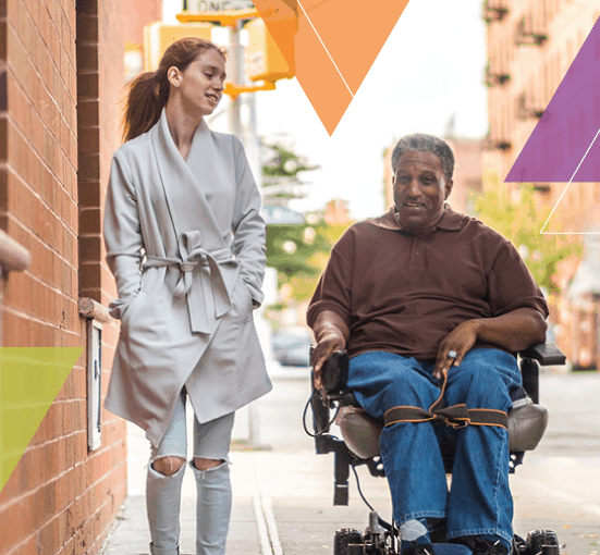 A travel trainer and a person who utilizes a wheelchair venture down a sidewalk after an ADA eligibility assessment for ADA certification. MTM Transit eligibility assessments and travel training through mobility management help people learn how to use public transit.
