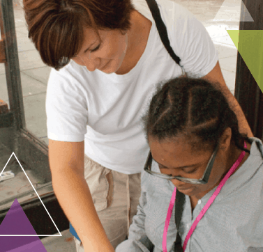 A woman stands behind another woman. Using MTM Transit eligibility assessments for ADA certification, she is helping the woman learn how to use public transit through our mobility management, ADA eligibility assessments, and travel training methods.