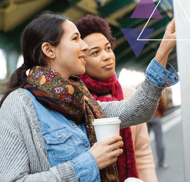 Two women point at a public transit map. The travel trainer is teaching the other woman about ADA eligibility, ADA certification, travel training, and mobility management.