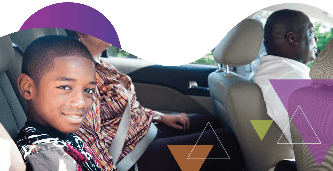 A young boy smiles at the camera from the back of a vehicle, while a woman sits beside him and a man drives the vehicle. MTM Transit offers reliable student transportation and special needs transportation to schools and programs serving children, including those covered by the McKinney-Vento Act.